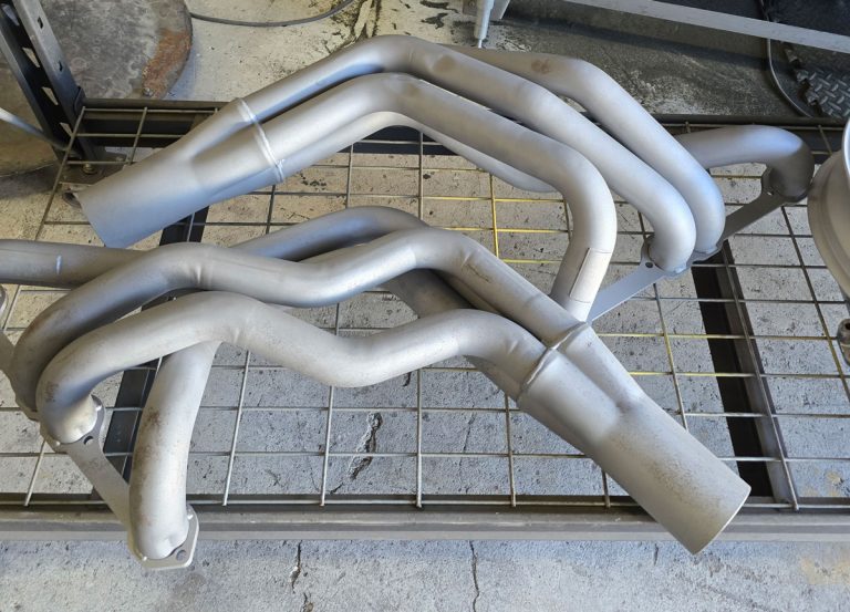 Pair of exhaust headers resting on a workshop rack