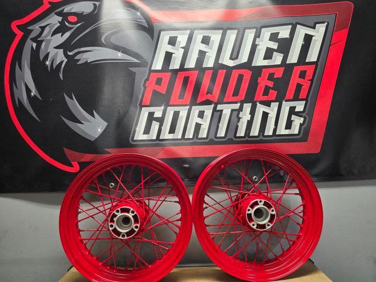 Pair of wire-spoke motorcycle wheels in front of the Raven banner